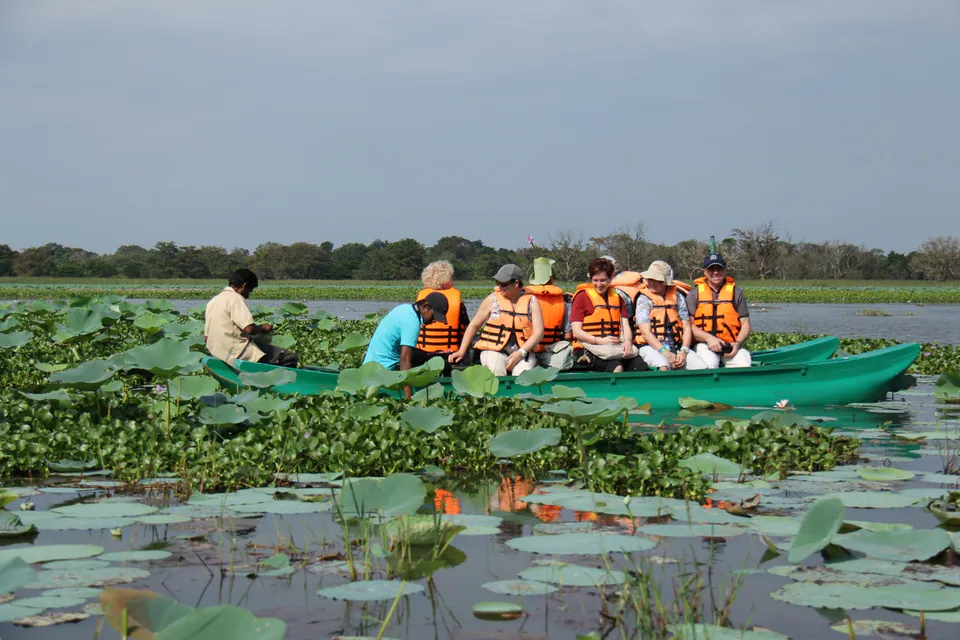 Travellers in life jackets on a wooden catamaran gliding through a tank covered in water lilies