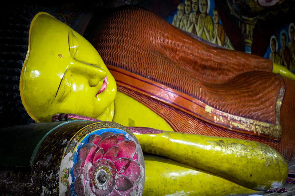 The glossy yellow face and rippled orange robe of a reclining Buddha, murals of disciples behind