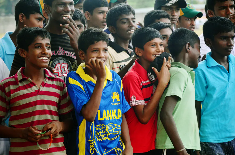 Schoolboys in cricket shirts laughing and cheering at a school cricket match
