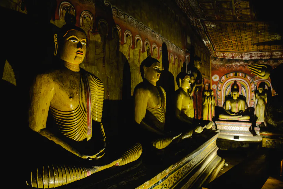 A row of painted seated Buddhas beneath frescoed walls inside a cave temple