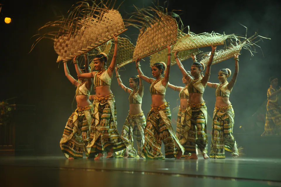 Dancers in batik costumes raising woven palm-leaf mats above their heads on a hazy stage