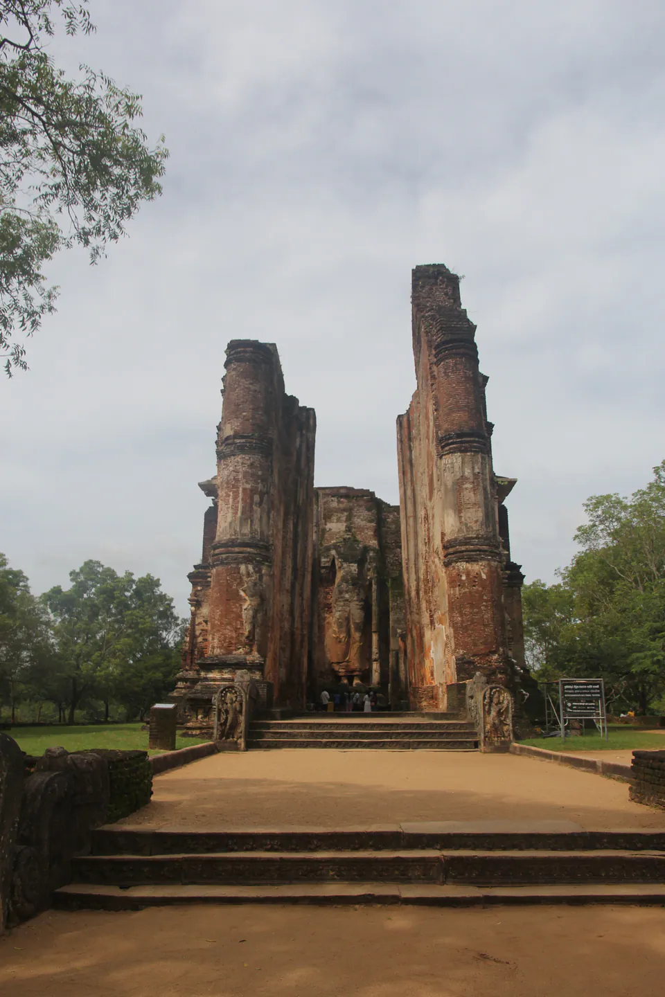 The towering brick walls of the Lankatilaka image house framing a standing Buddha, reached by carved stone steps