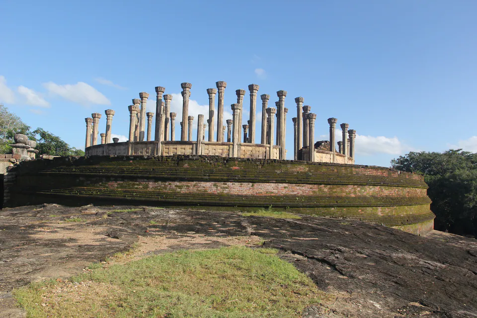 Concentric rings of stone pillars on the circular brick terrace of an ancient relic house, under a blue sky