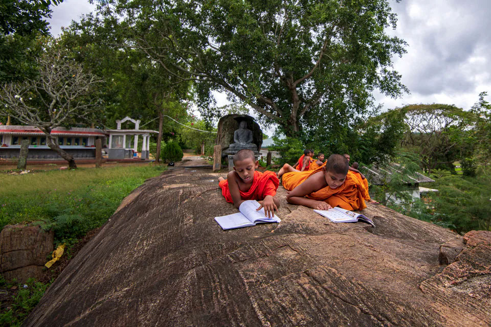Young novice monks lying on a granite rock in the temple grounds to study their books