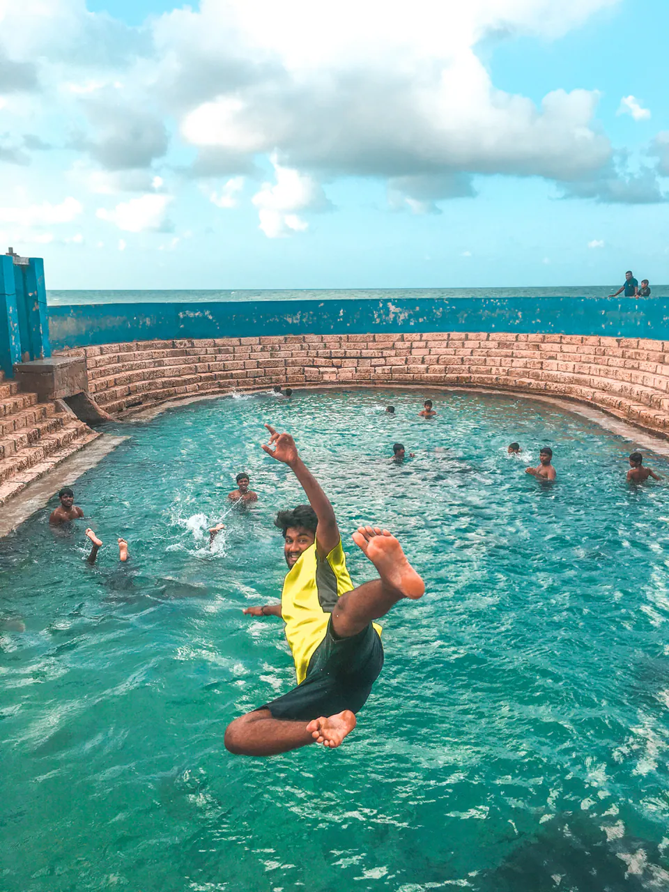 A young man leaping into a turquoise seaside bathing pool, the ocean beyond