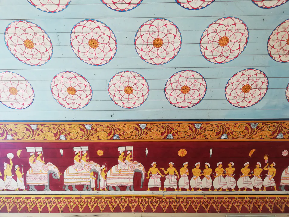 A temple ceiling painted with lotus roundels above a frieze of a procession of drummers and flag-bearers