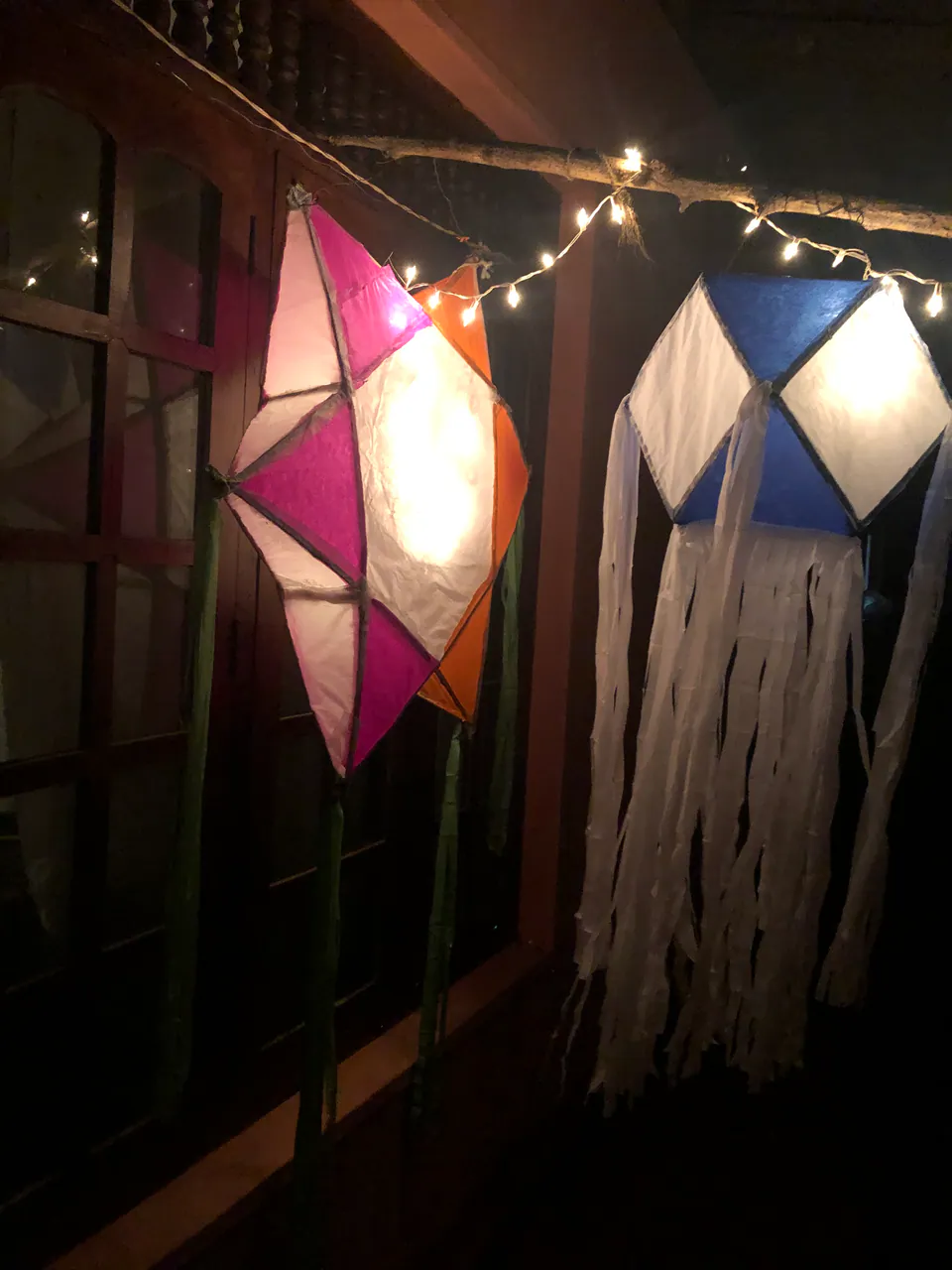 Handmade paper Vesak lanterns glowing under fairy lights on a veranda at night
