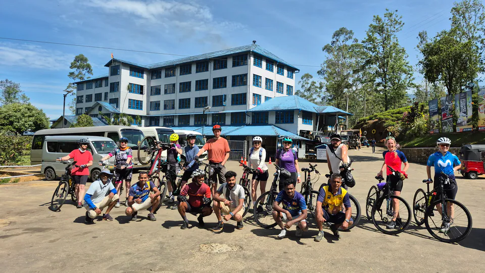 A cycling group and their Sri Lankan crew with bikes and support vehicles outside a tea factory