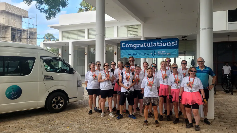 A charity cycling group with finisher medals celebrating beside their support van