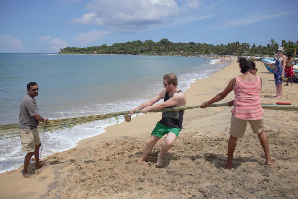 Travellers helping a fisherman haul a beach-seine rope on a sandy bay