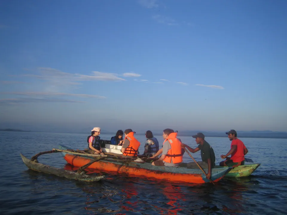 Travellers in life jackets aboard an outrigger canoe paddled by local fishermen on a calm lagoon at dawn