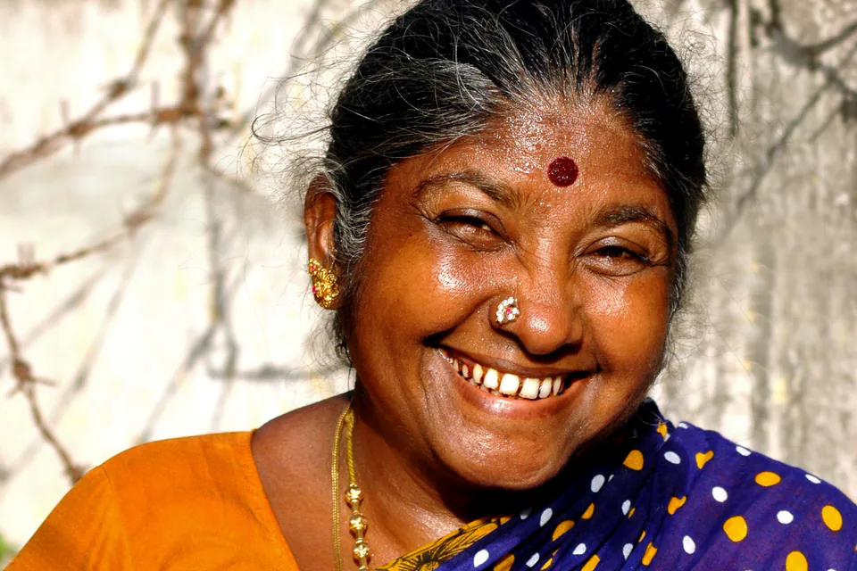 A smiling woman in a blue polka-dot sari with a red pottu and gold earrings