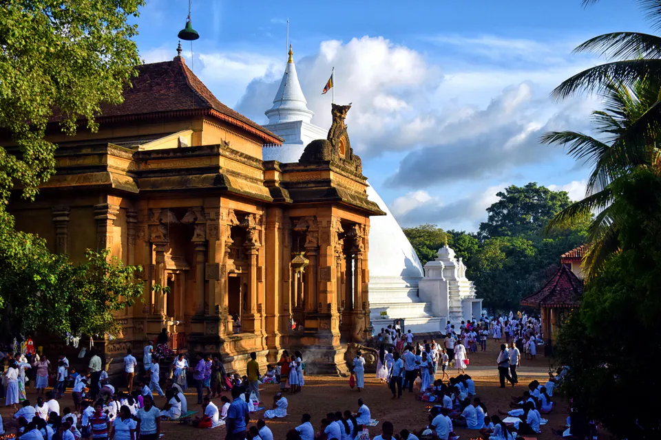 Devotees in white gathered before the ornate image house and stupa of Kelaniya temple in golden light