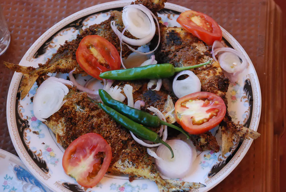 A plate of spiced fried fish with tomato, onion rings and green chillies