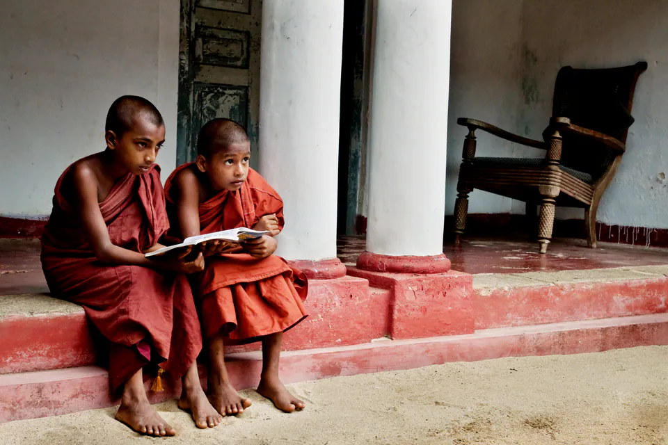 Two young novice monks sharing a book on the red step of a pillared temple verandah