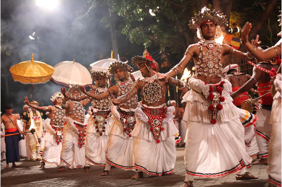 Kandyan dancers in silver-beaded costumes performing at night in the Esala Perahera