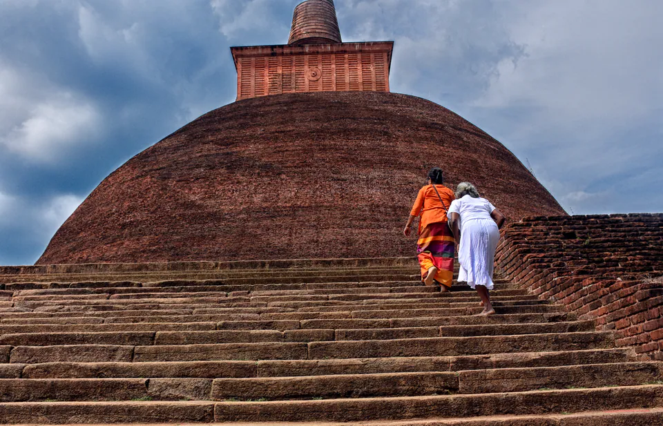 Two women pilgrims climbing the broad stone steps of a giant brick dagoba