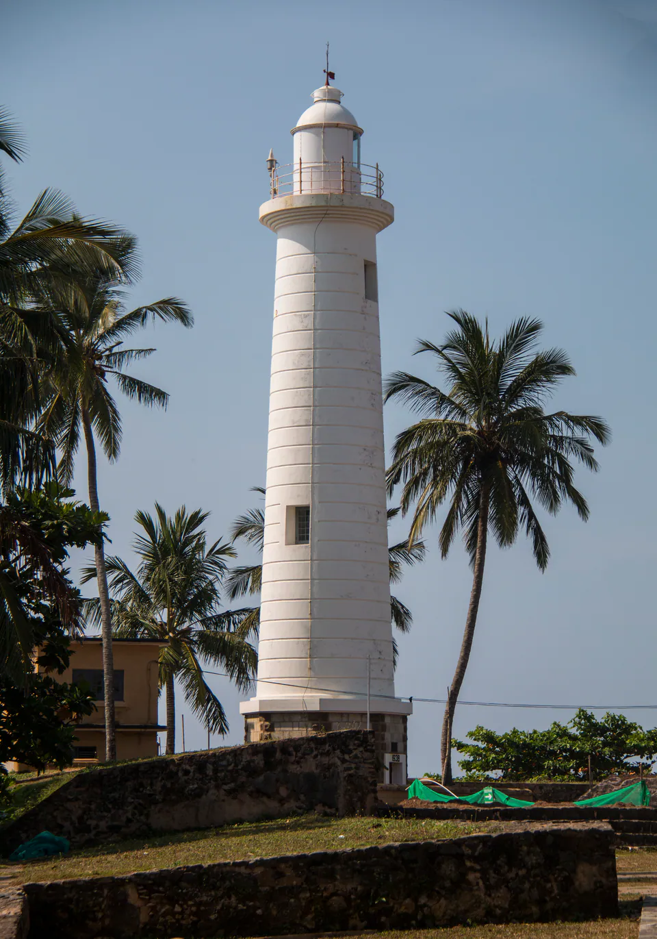 The white lighthouse of Galle Fort among coconut palms above the rampart