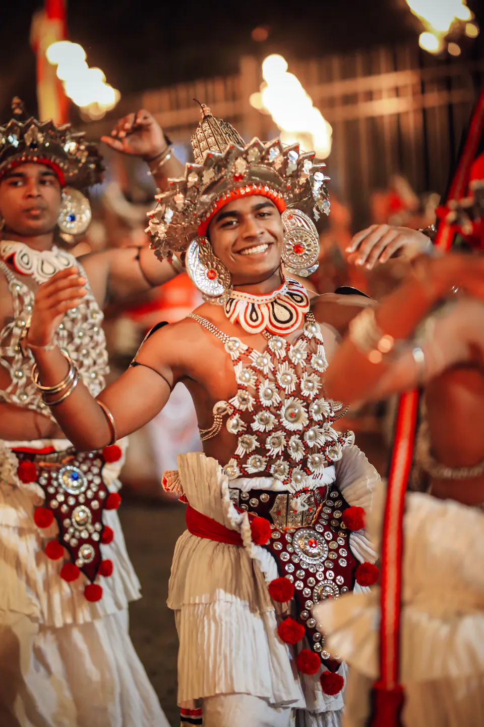 A smiling Kandyan dancer in traditional costume lit by torchlight