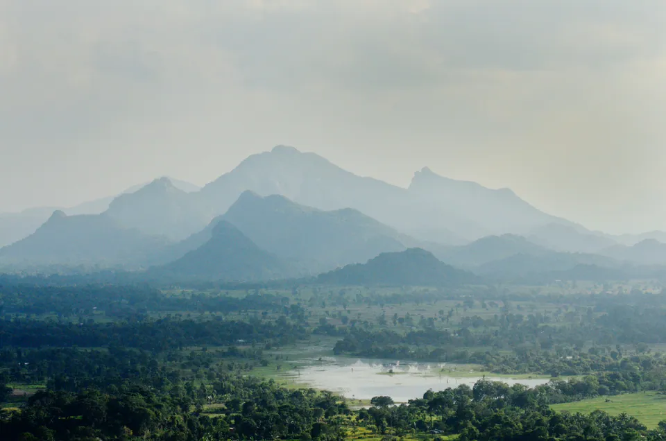 Hazy layered ridges of the central highlands above lowland forest and a small reservoir