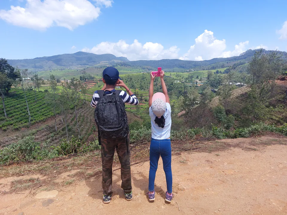 A parent and child at a viewpoint over rolling tea estates, seen from behind