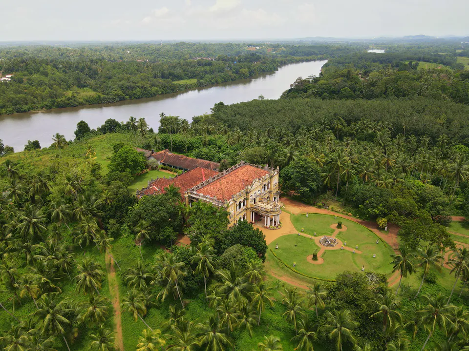 A colonial-era mansion with a circular garden among coconut groves beside a wide river, seen from the air