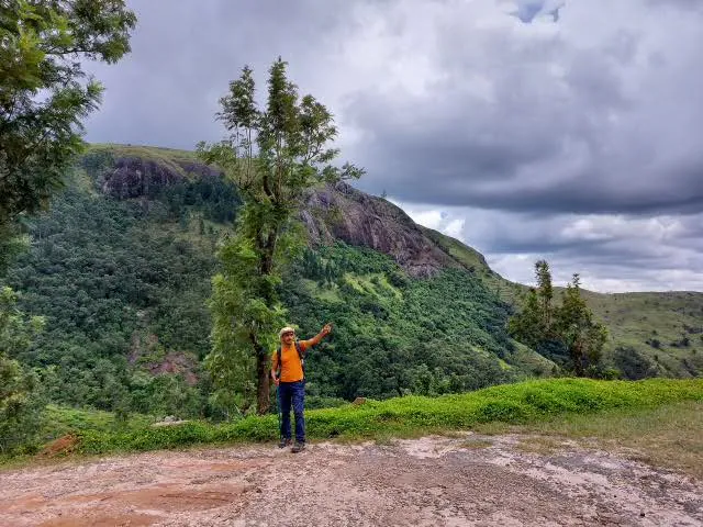 A guide on a rock slab pointing out a forested granite escarpment under brooding clouds