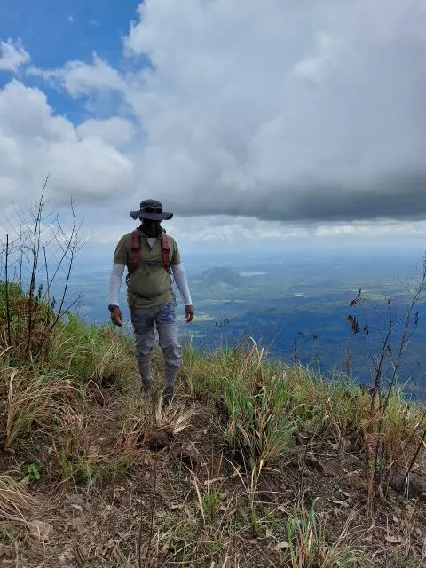 A walker in a wide-brimmed hat on the grassy edge of the Uva escarpment